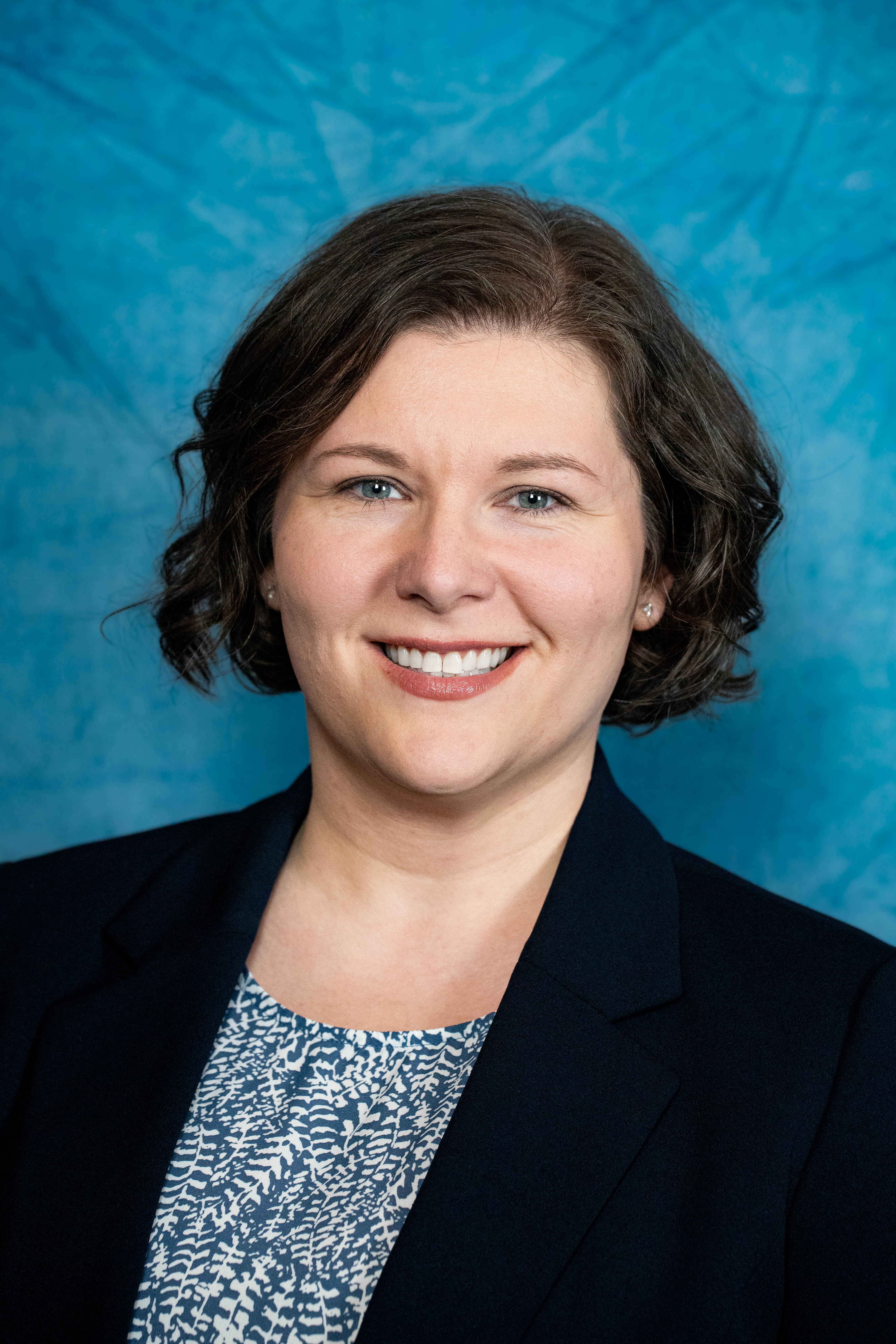 City council headshot — dark blazer, curly bob